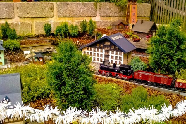 Charming miniature train in a detailed garden setting with model buildings and greenery.